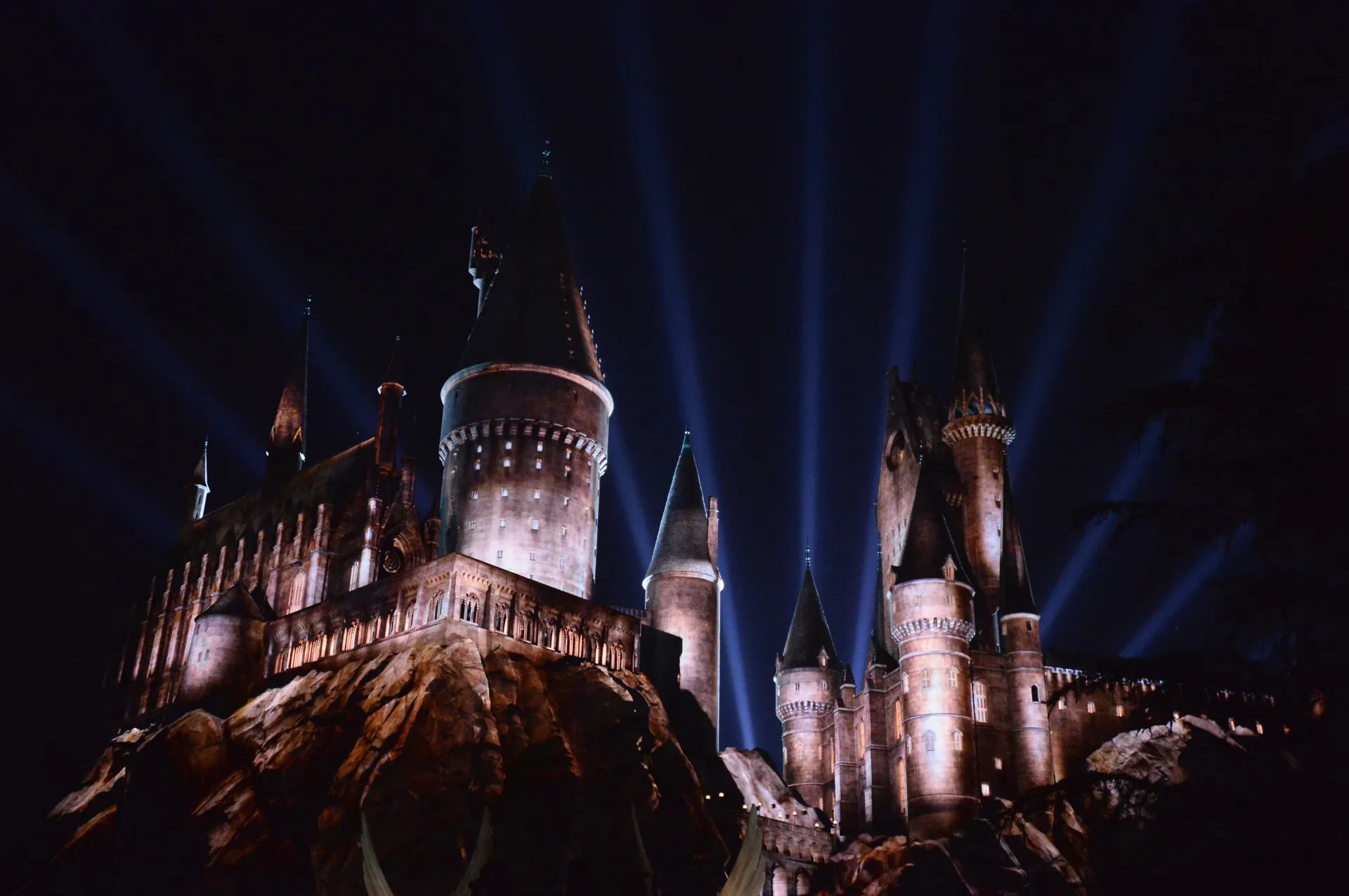 O castelo de Hogwarts no parque da Universal Studios iluminado com luzes coloridas à noite.