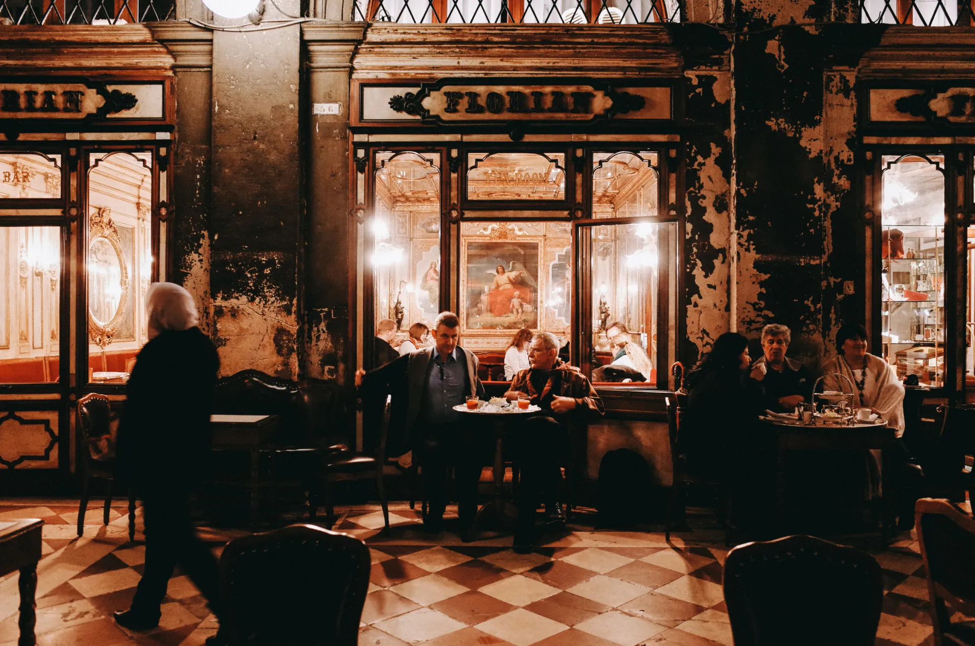 O opulento salão do Caffè Florian em Veneza, com afrescos no teto e garçons de uniforme branco.