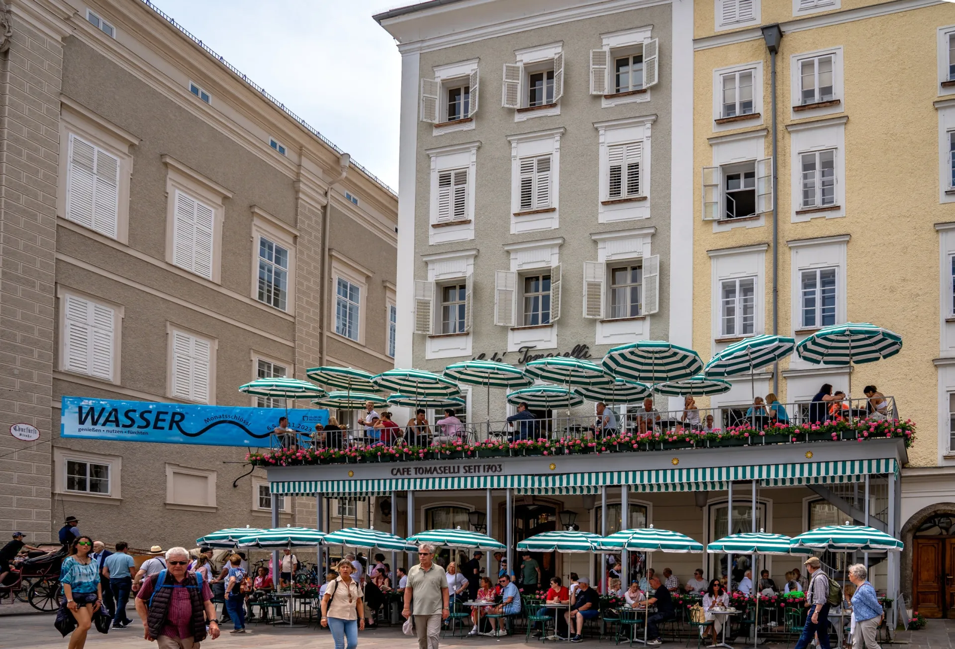 O icônico Café Tomaselli em Salzburgo, com suas tendas listradas de verde e branco e mesas ao ar livre.
