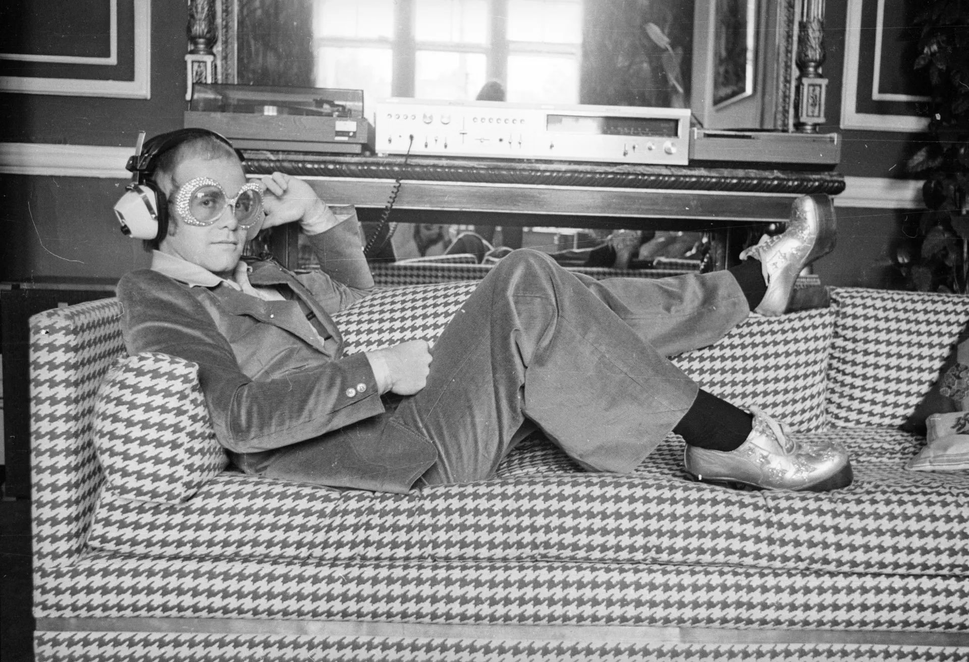 Elton John sorrindo, usando um de seus famosos óculos coloridos.
